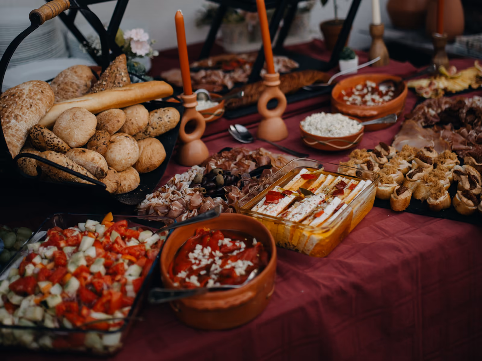 An event buffet table laid with breads, salads, cured meats and finger food beside tall candles